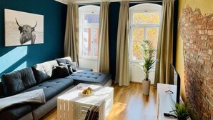 A modern living room with a dark blue wall, a black sofa, a white coffee table with books, a potted plant, and a brick wall. - Industrial Style Dresden (Dresden)