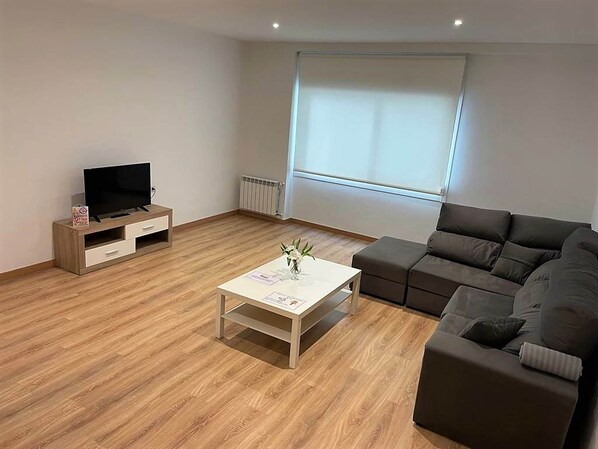A modern living room with a wooden floor, a flat-screen TV on a wooden stand, a grey sofa, and a white coffee table. - Apartment in Ourense Near Thermal Baths (Ourense)