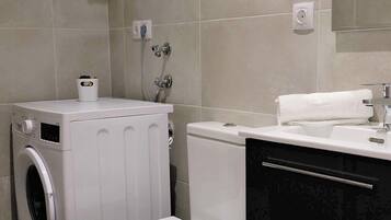 A compact bathroom with a washing machine, toilet, and sink.