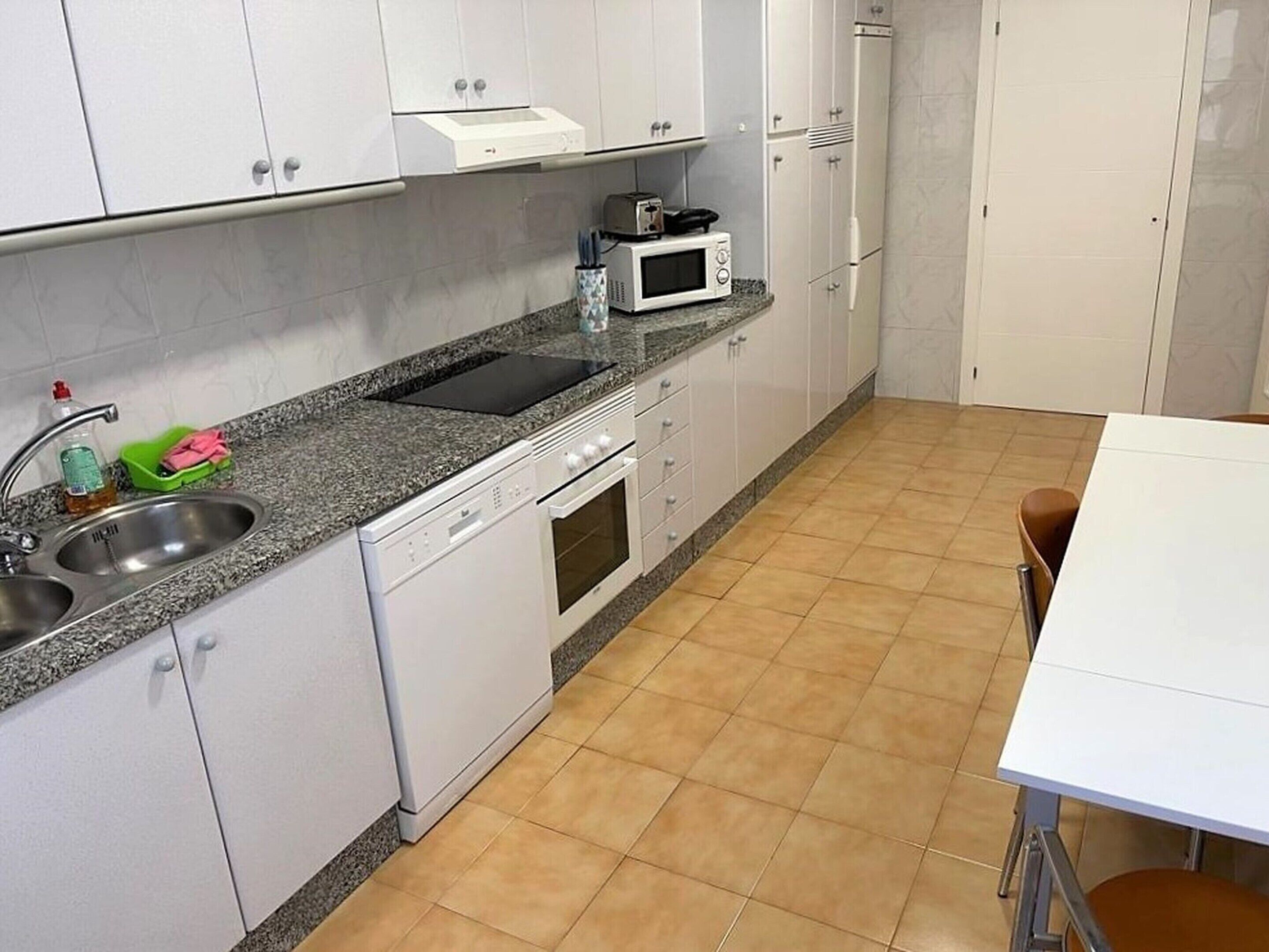 Een keuken met witte kasten, een granieten aanrecht, een spoelbak, een magnetron en een fornuis.