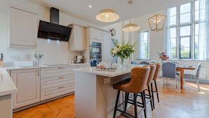 Una cocina moderna con armarios blancos, una isla central, taburetes de bar y una zona de comedor con mesa y sillas.