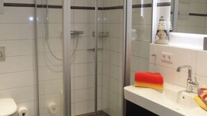 A modern bathroom with a glass shower enclosure, a white sink with a red towel, and a mirror above the sink. - Lutje Sandbank Modern Retreat (Juist)