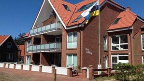 A two-story building with a red-tiled roof, a balcony on the upper floor, and a flagpole with a flag. - Lutje Sandbank Modern Retreat (Juist)