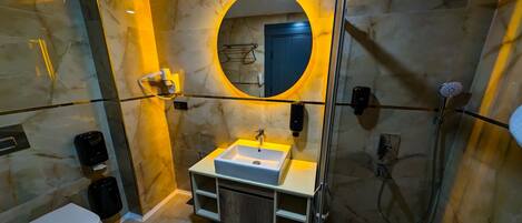 Un baño moderno con piso de mármol, un espejo redondo, un lavamanos, un inodoro y una ducha.