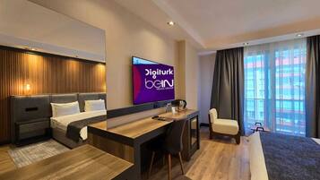 A modern hotel room with a bed, a desk, a chair, and a television displaying 'Digiturk Bein'.