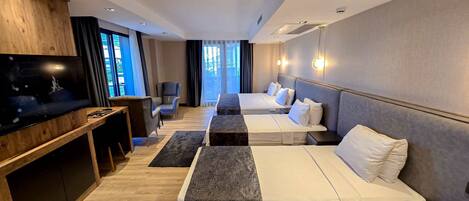 A modern hotel room with a flat-screen TV, a desk, two beds, a sofa, and a large window with curtains.
