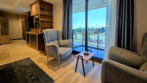 A modern living room with a large window, a grey armchair, a small table, and a wooden bookshelf.