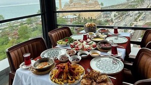 A table set for a meal with various dishes, a view of a mosque with two minarets, and a cityscape in the background.
