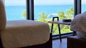 A room with a large window offering a view of the sea, a wooden table, and a plush chair.