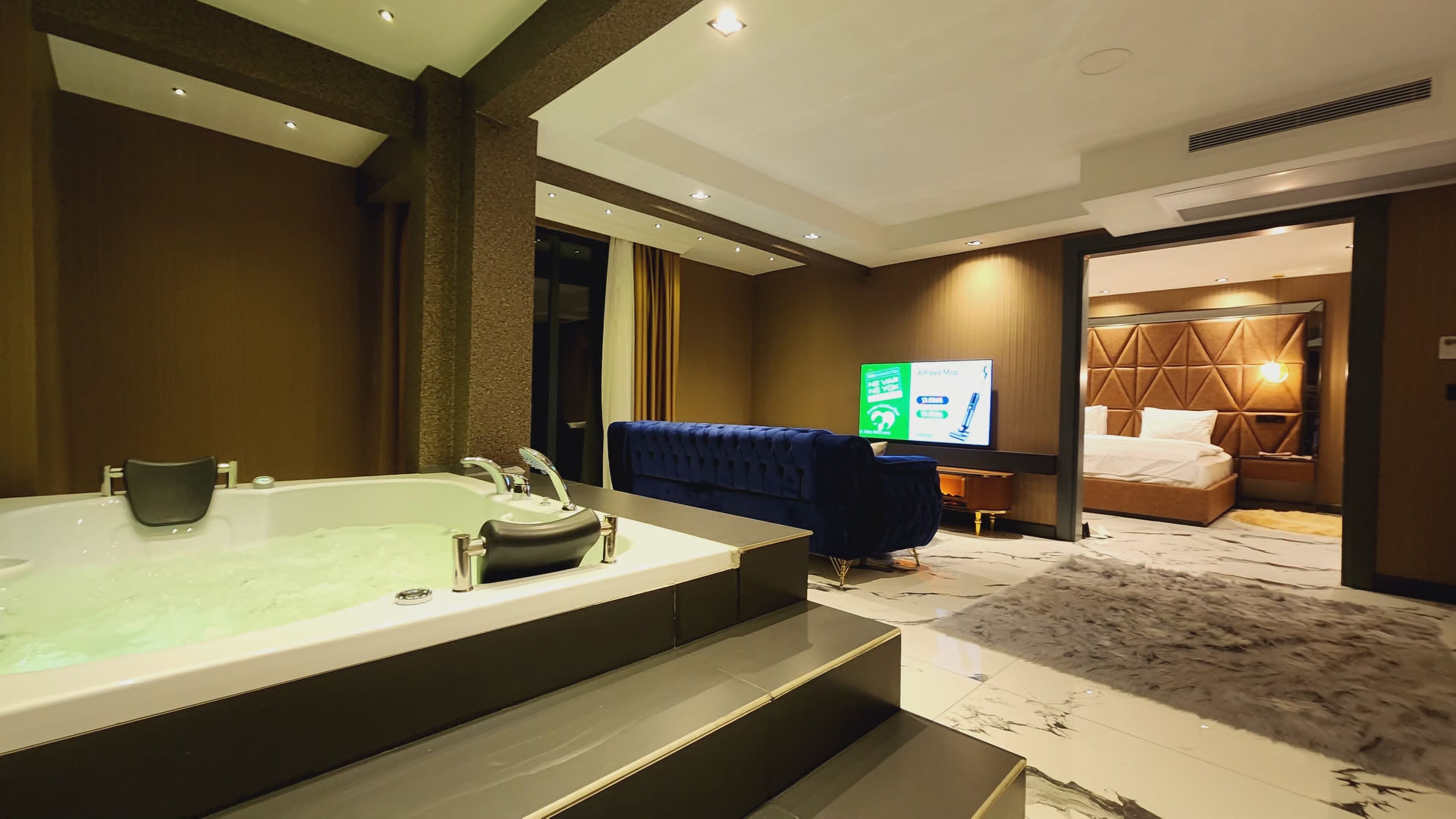 A hotel room with a large bathtub, a sofa, a bed with a headboard, and a television displaying a map.