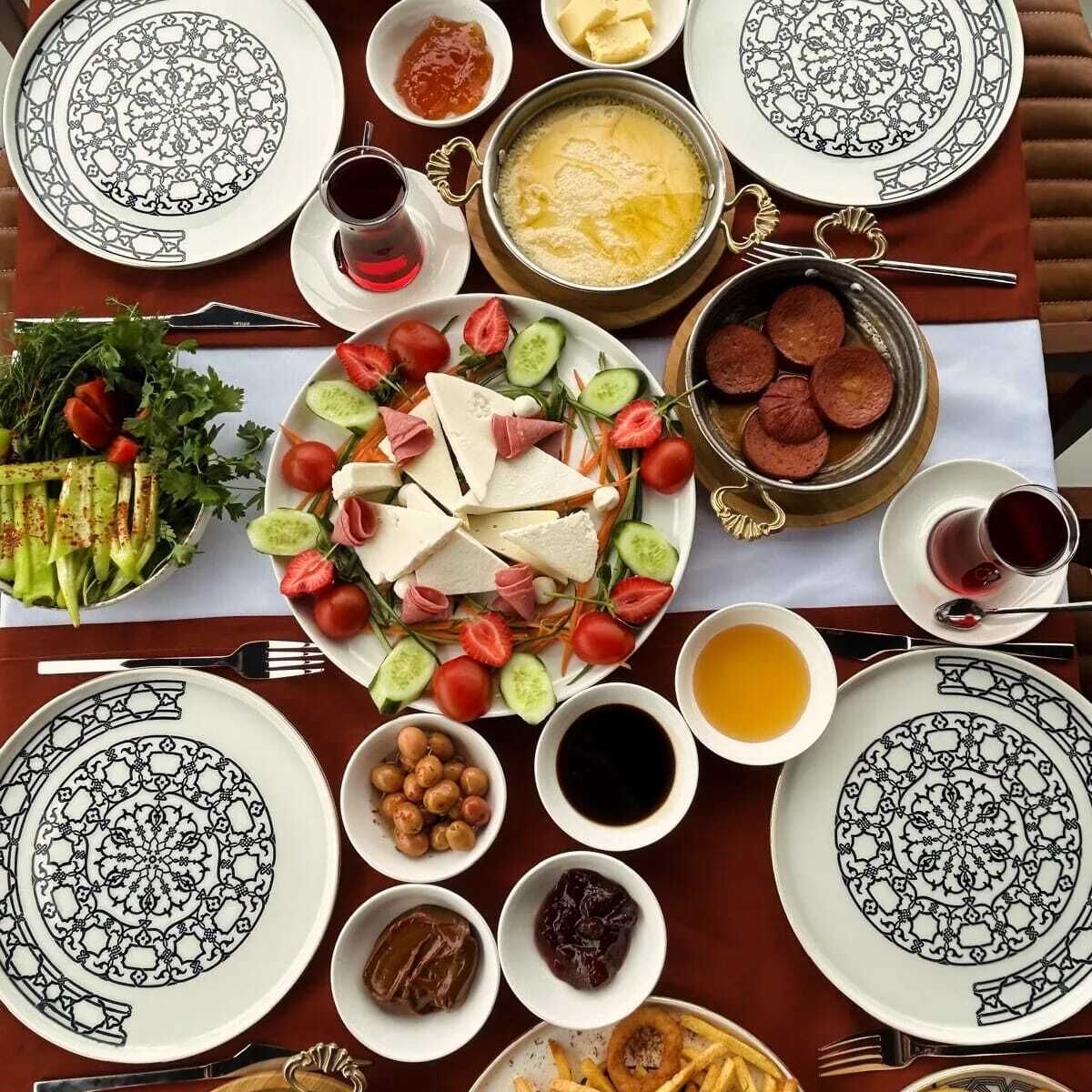 Une table dressée avec différents plats, notamment une salade, du fromage, des olives et un pot de soupe.
