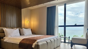 A modern hotel room with a large bed, a view of the sea, and a balcony with a chair.
