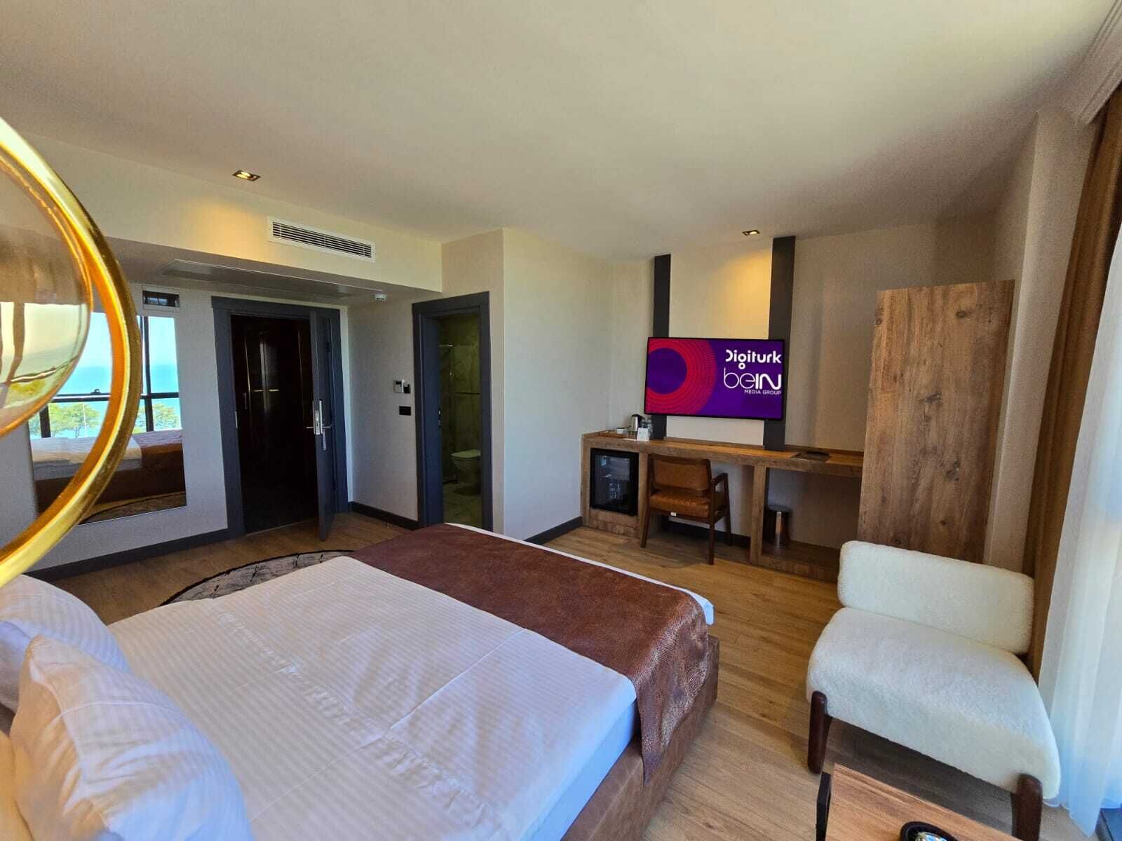 Quarto de hotel com cama, escrivaninha, computador, televisão e guarda-roupa.