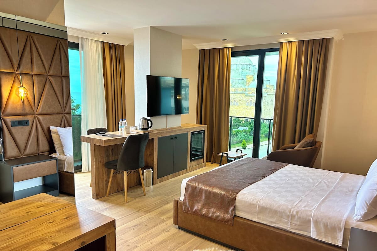 Ein modernes Hotelzimmer mit einem großen Bett, einem Schreibtisch mit Stuhl, einem Fernseher und Blick auf ein historisches Gebäude durch die Fenster.