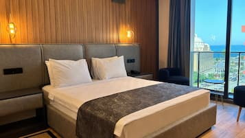 Ein Hotelzimmer mit einem großen Bett, Holzwandverkleidung und einem Balkon mit Blick auf die Stadt und das Meer.