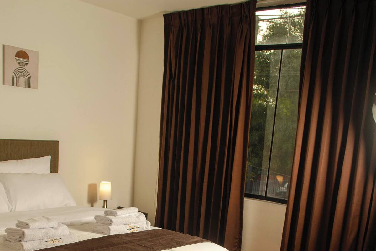 A hotel room with a neatly made bed, a bedside lamp, and a window with curtains.