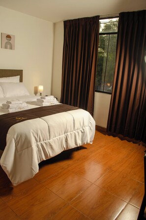 A hotel room with a neatly made bed, a bedside lamp, and a window with curtains. - SOUL GARDEN HOTEL (Arequipa)