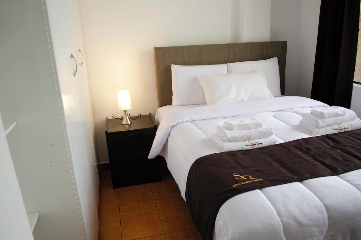 A hotel room with a neatly made bed, a nightstand with a lamp, and a brown headboard.