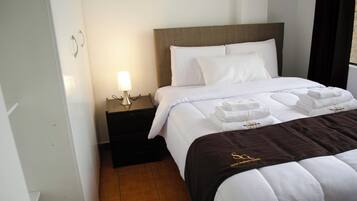 Quarto de hotel com uma cama bem arrumada, uma mesa de cabeceira com abajur e cabeceira marrom.