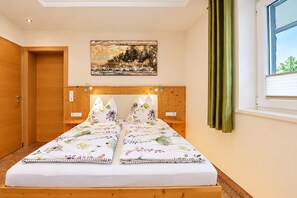 A bedroom with a wooden headboard, a bed with floral bedding, a painting on the wall, and a window with curtains. - Apartment in Mittersill Near ski Lift (Mittersill)