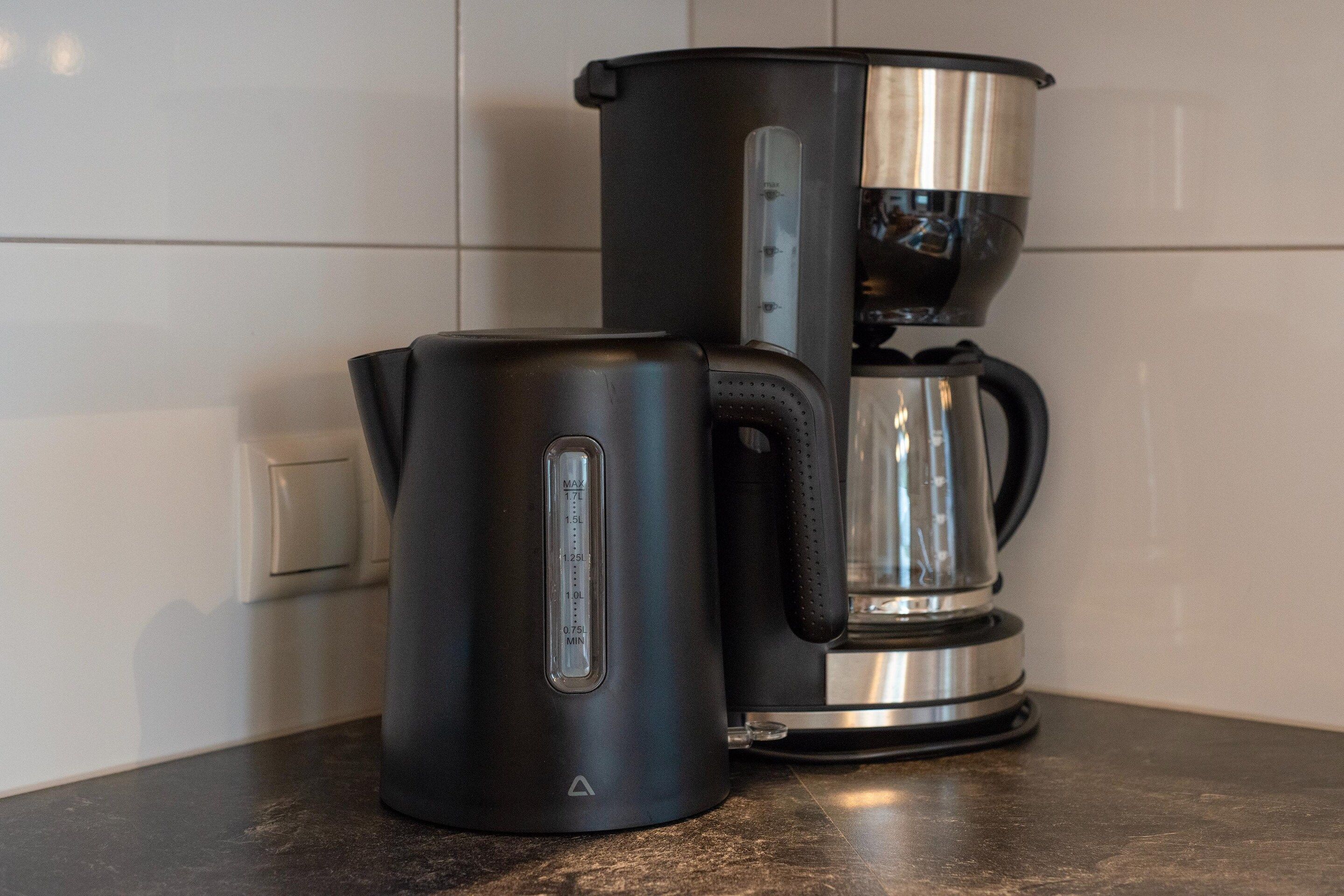 En svart elektrisk vattenkokare och en kaffebryggare i rostfritt stål står på en köksbänk.