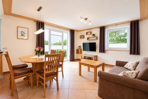 A modern living room with a wooden dining table, chairs, a sofa, a TV, and a balcony with curtains. - Apartment in Mittersill Near ski Lift (Mittersill)