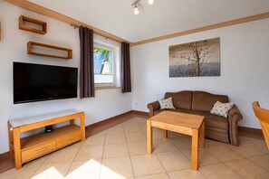 A living room with a flat-screen TV, a wooden coffee table, a brown sofa, and a painting on the wall. - Apartment in Mittersill Near ski Lift (Mittersill)