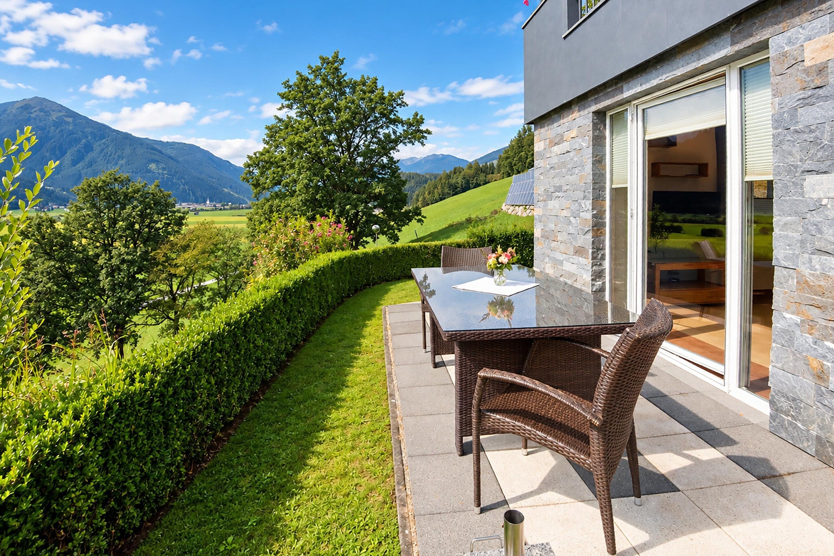 An outdoor patio with a table and chairs, a stone wall, and a view of a green landscape with mountains in the background.