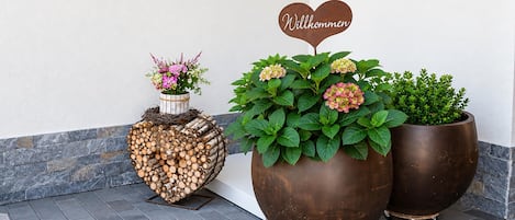 A decorative arrangement of potted plants and a heart-shaped sign with 'Welcome' on a building's exterior.