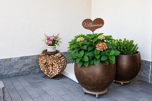 Une composition décorative composée de plantes en pot et d’une enseigne en forme de cœur portant l’inscription « Bienvenue », placée sur la façade d’un bâtiment.