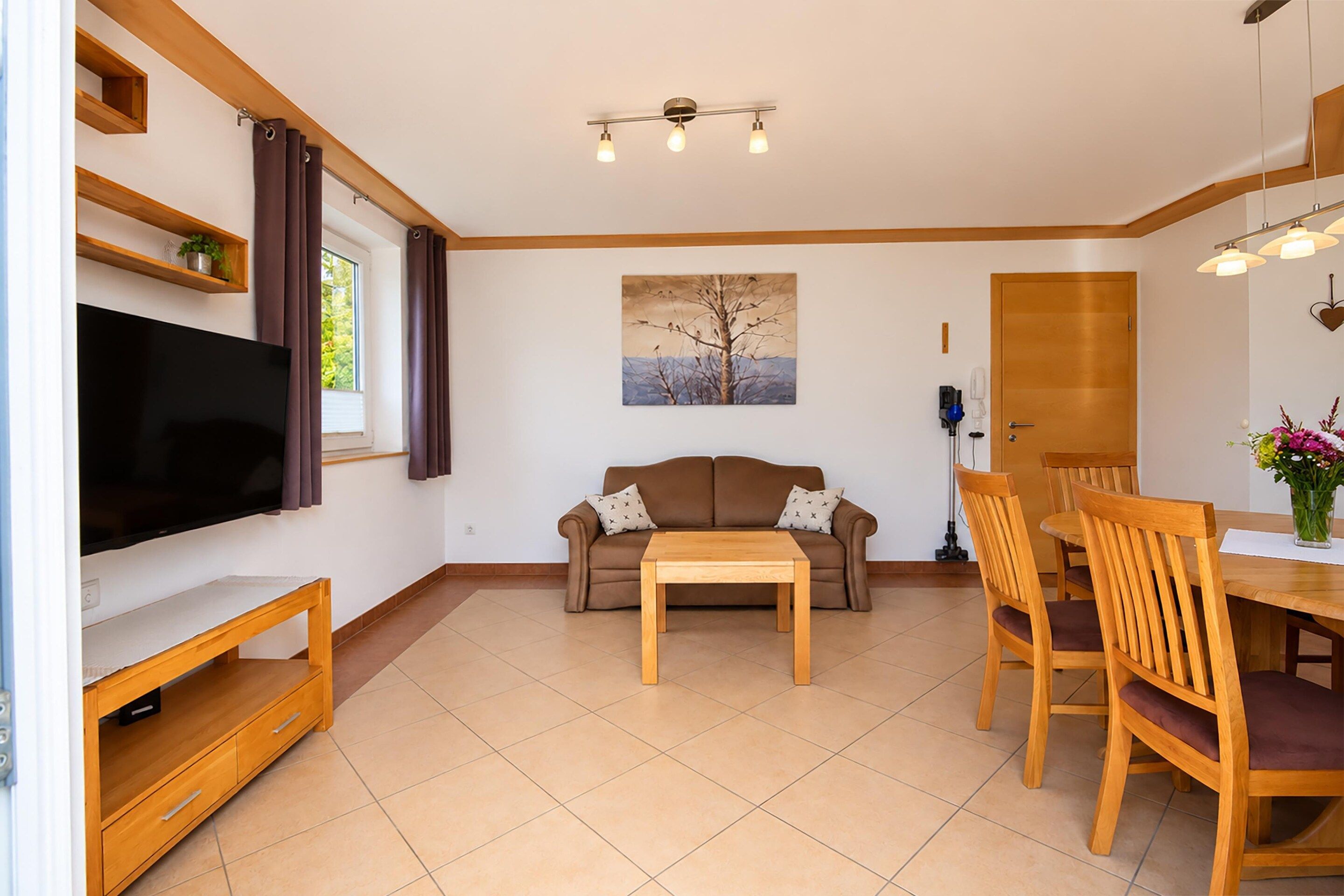 Ein Wohnzimmer mit Flachbildfernseher, braunem Sofa, Couchtisch aus Holz und Essbereich mit Holztischen und einer Tafel.