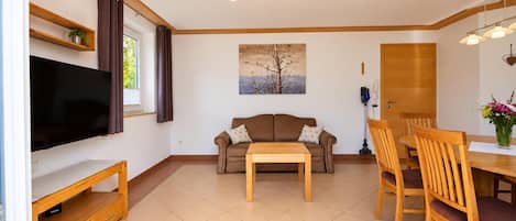 Una sala de estar con un televisor de pantalla plana, un sofá marrón, una mesa de centro de madera y un comedor con sillas y una mesa de madera.