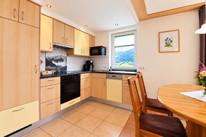 A modern kitchen with wooden cabinets, a black stove, and a window with a mountain view. - Apartment in Mittersill Near ski Lift (Mittersill)