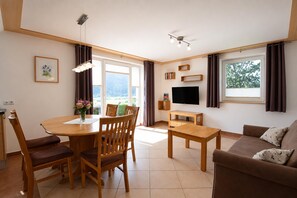 A modern living room with a dining area, a flat-screen TV, and a large window with curtains. - Apartment in Mittersill Near ski Lift (Mittersill)