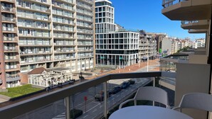 A high-rise building with multiple balconies, a modern glass structure, and a view of a street with cars.