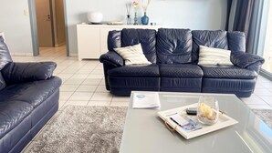 A modern living room with a dark blue leather sofa, a glass coffee table, and a white cabinet.