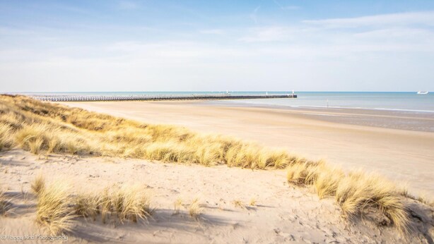 A beach with sand dunes and a pier extending into the water.