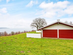 A single-story building with a red garage door, a white fence, and a tree in the background. - 4 Star Holiday Home in Aabenraa (Aabenraa)