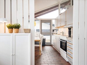 A narrow kitchen with white cabinets, a stove, and a dining area with a table and chairs. - 4 Star Holiday Home in Aabenraa (Aabenraa)