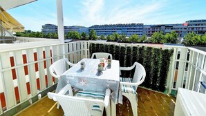 A balcony with a table and chairs, a view of buildings in the background, and a clear sky. - Holiday Home Near Spiaggia Tartaruga (Caorle)