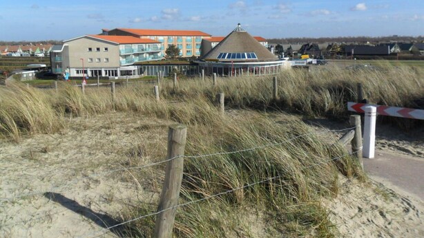 A coastal building with a red roof, a large window, and a sandy foreground with a fence. - Holiday Home Seestern 283 (Julianadorp)