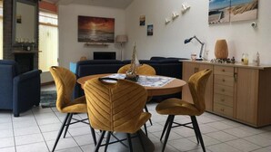 A modern living room with a round dining table, yellow chairs, a sofa, and a TV. - Holiday Home Seestern 283 (Julianadorp)