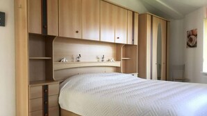A bedroom with a bed, wooden wardrobe, and shelving units. - Holiday Home Seestern 283 (Julianadorp)