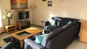 A living room with a sofa, a coffee table, a TV, and artwork on the wall. - Holiday Home Seestern 283 (Julianadorp)