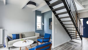 A modern living room with a grey sofa, blue chairs, a white coffee table, and a black spiral staircase. - Fischer Heiligenhafen 4c (Heiligenhafen)