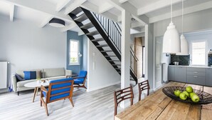 A modern kitchen with a wooden table, a staircase, and a dining area with blue chairs. - Fischer Heiligenhafen 4c (Heiligenhafen)