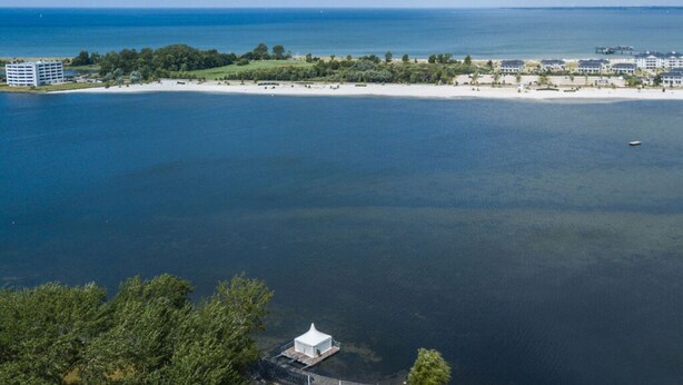 A coastal hotel with a beach view, a white gazebo, and a marina. - Fischer Heiligenhafen 4c (Heiligenhafen)