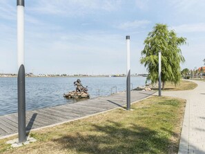 A waterfront walkway with a statue, a wooden dock, and a grassy area.