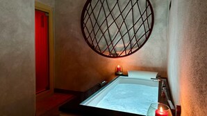 Une salle de spa dotée d’une grande baignoire, d’une fenêtre ronde et d’une porte rouge.