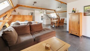 A spacious loft apartment with a high ceiling, exposed wooden beams, a dining area, kitchenette, and a large wardrobe. - Cottage on Sheep Farm With Gelateria (Merksplas)